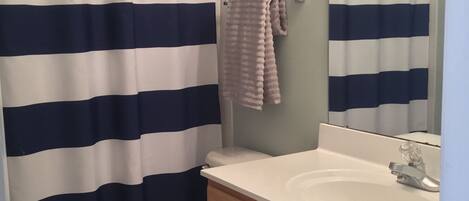 A bathroom with a striped shower curtain, a toilet, a sink with a mirror, and wooden cabinets.