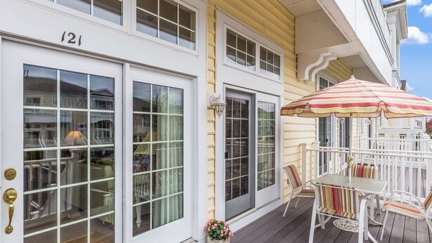 Une maison à deux étages avec un porche, une table à manger avec des chaises et un parasol à rayures.