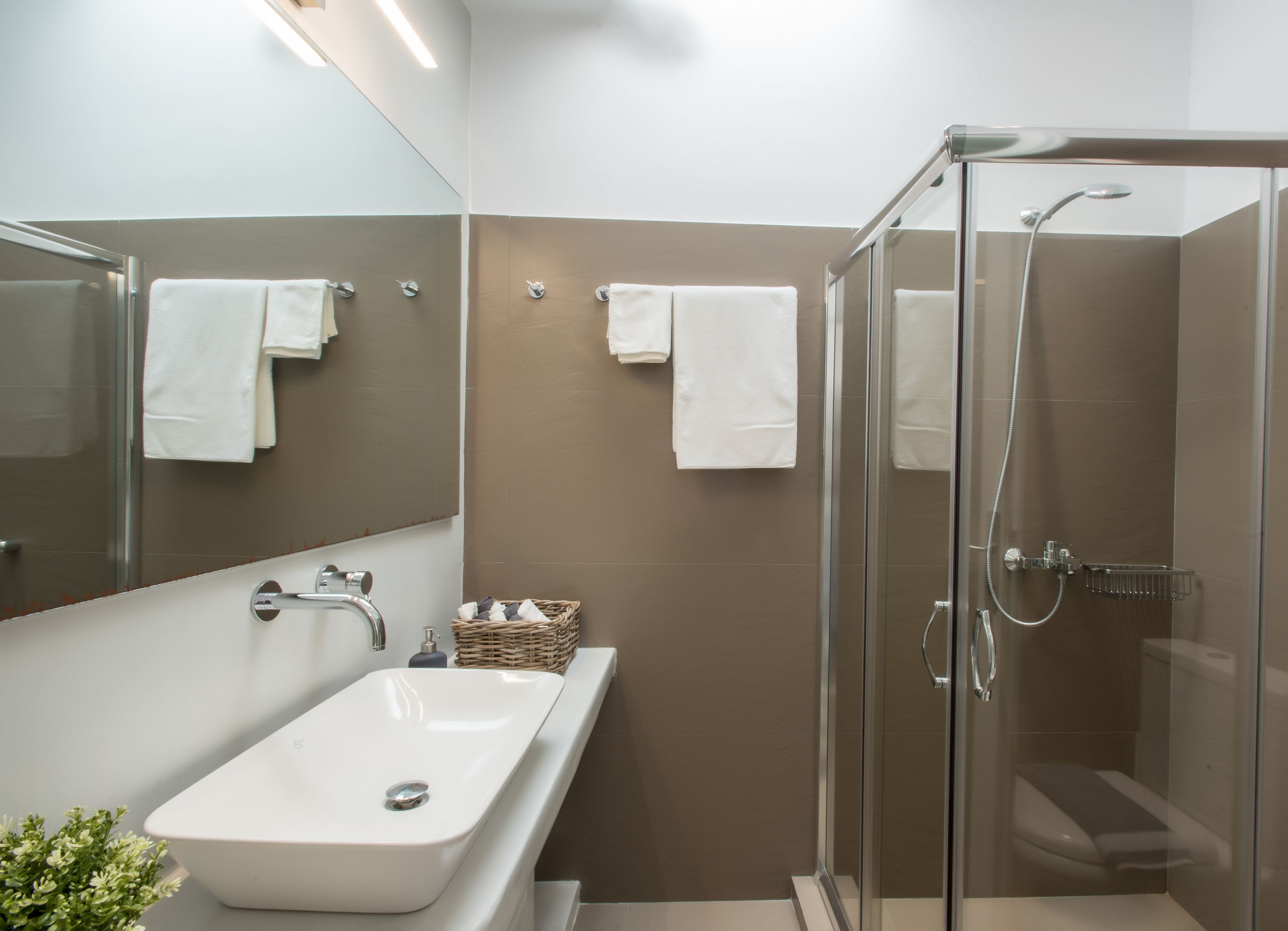 Un bany modern amb dutxa d'envidriament, un lavabo blanc i un mirall gran.