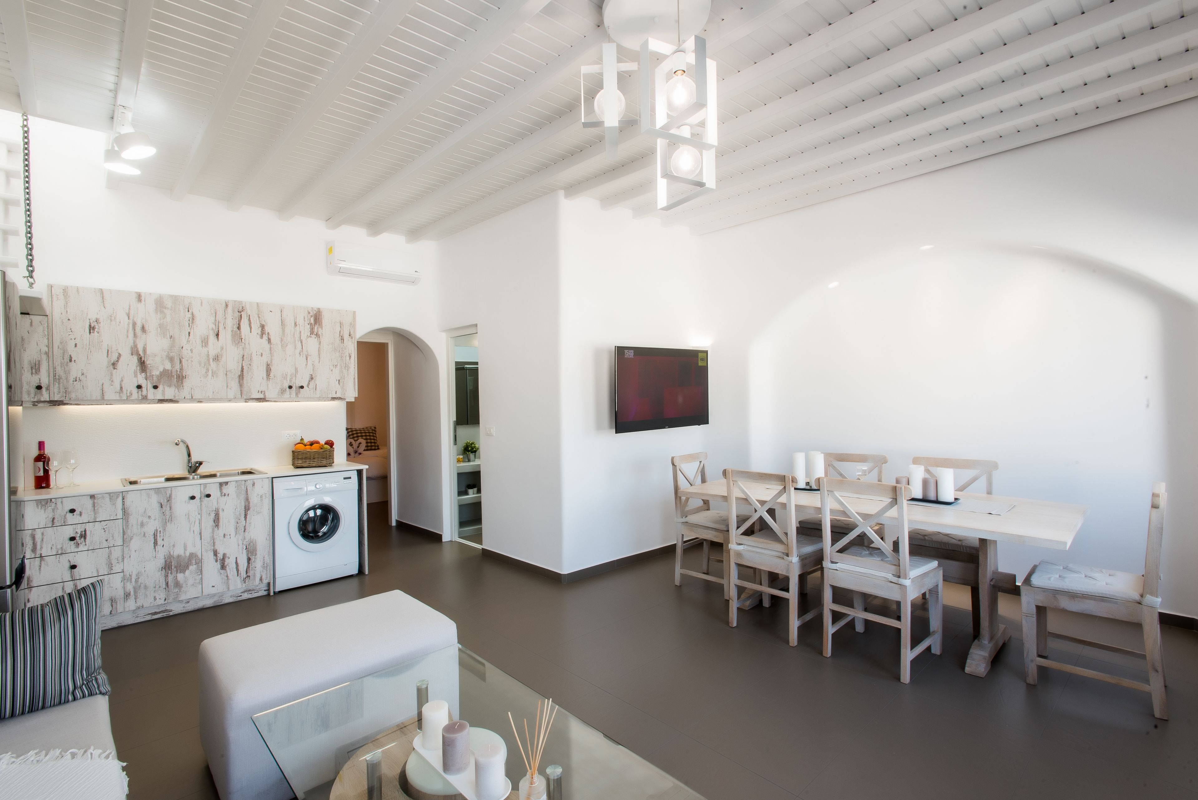 Una cocina moderna con armarios blancos, lavadora integrada y un comedor con sillas y mesa de madera.