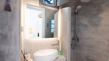 Un baño con lavamanos blanco, un espejo, ducha y un perchero para toallas.