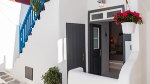 Eine enge Straße mit einem weißen Gebäude, einer blauen Treppe und einer Tür zu einem Zimmer mit einem Bett und einer hängenden Pflanze.