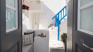 Ein schmaler Flur mit einer weißen Tür, einer blauen Treppe und einer kleinen Sitzecke mit Kissen und Tablett mit Glas und Kerze.