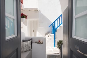 Un pasillo estrecho con una puerta blanca, una escalera azul y una pequeña zona de estar con un cojín y una bandeja con un vaso y una vela.