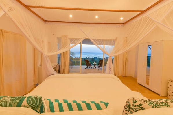 Un dormitorio con una cama grande, cortinas blancas y vistas al mar a través de amplias ventanas.