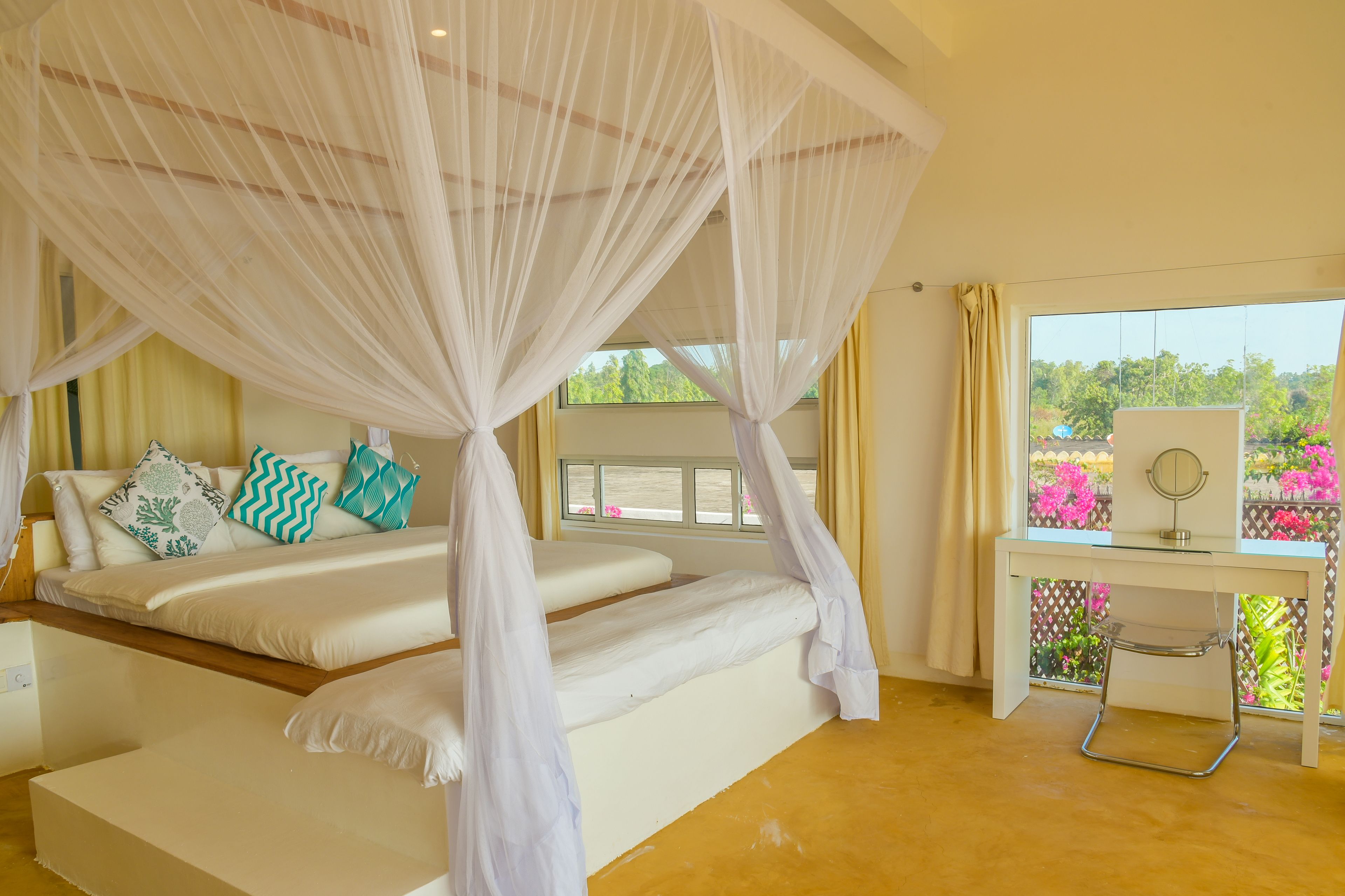 Un dormitorio con cama a dosel, un escritorio con espejo y vistas al verdor exterior.