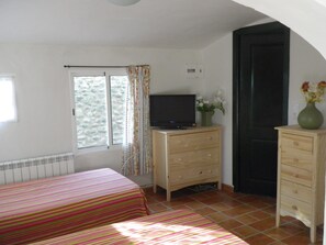 Een slaapkamer met twee bedden, een televisie op een houten dressoir, een raam met gordijnen en een deur.