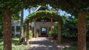 A stone pathway leading to a building with a covered entrance, surrounded by tropical plants and trees. - Diani Blue (Diani Beach)