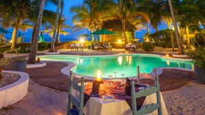 A poolside dining area with a table set for two, surrounded by palm trees and a pool. - Diani Blue (Diani Beach)