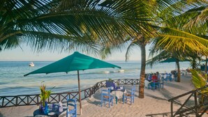 A beachside restaurant with outdoor seating, palm trees, and a view of the ocean. - Diani Blue (Diani Beach)