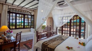 A bedroom with a large bed, a wooden chair, a table with a lamp, and a window with a view of the outdoors. - Diani Blue (Diani Beach)
