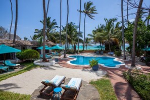 A pool area with lounge chairs and umbrellas, surrounded by palm trees and a view of the ocean.