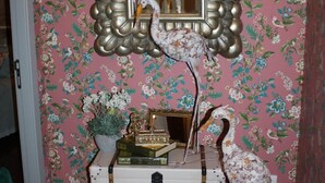 Una habitación con papel tapiz floral, un espejo con marco decorativo y una escultura de un pájaro sobre una pila de maletas.