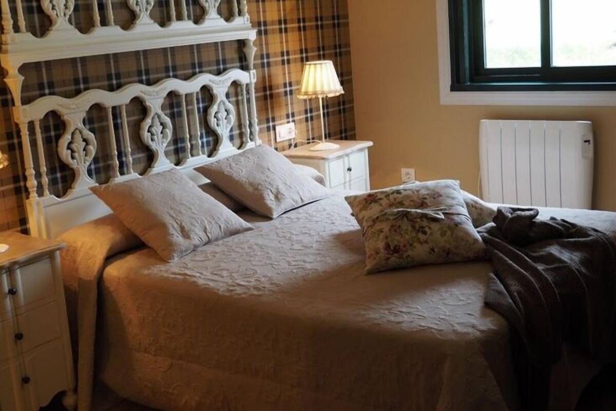 Una cama con un almohadón floral, una lámpara de noche y un cabecero estampado.