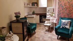 Una cocina compacta con comedor, un sillón verde azulado y una mesita con una planta.