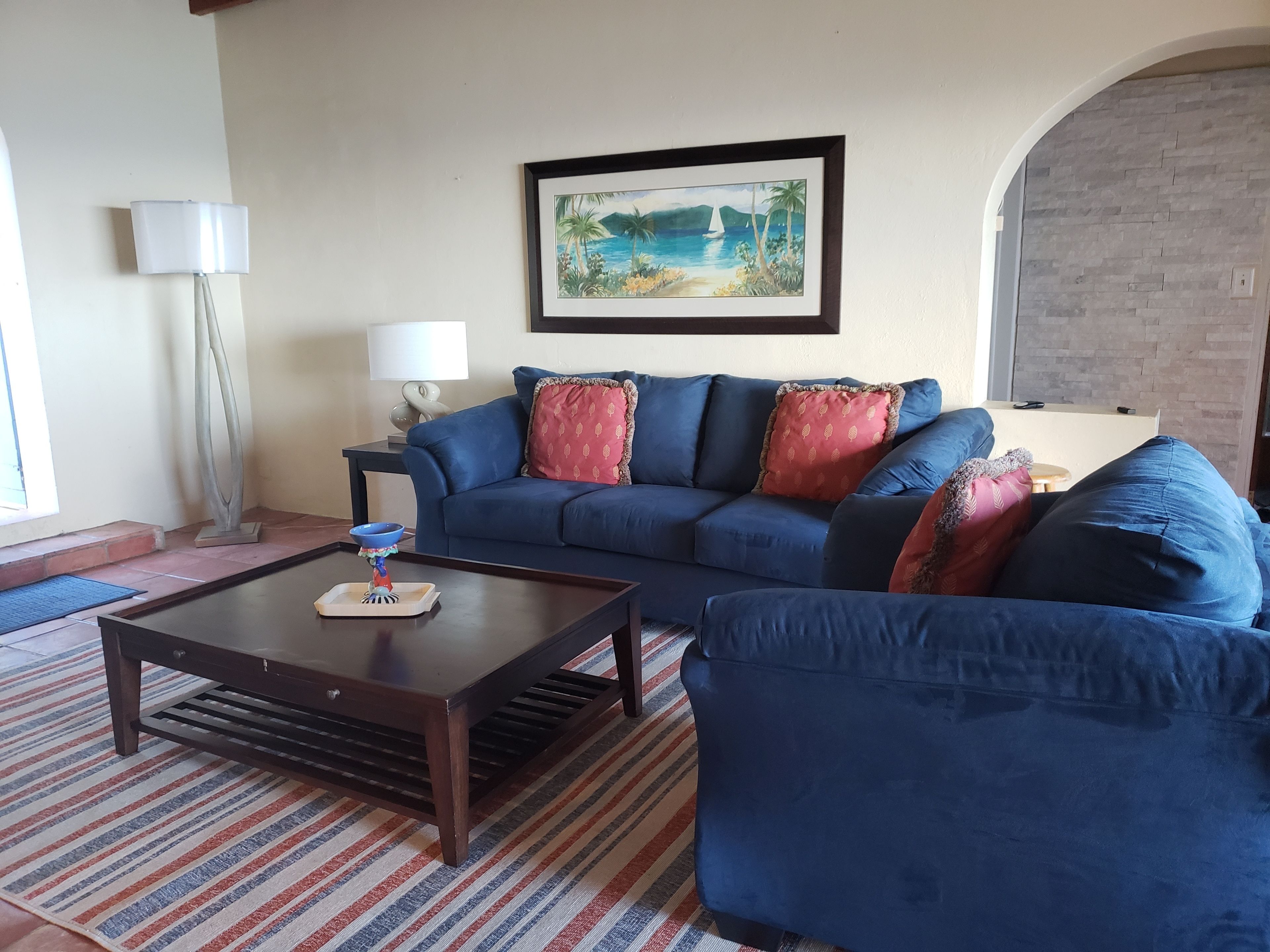 Un salón con un sofá azul, una mesa de centro y un cuadro en la pared.