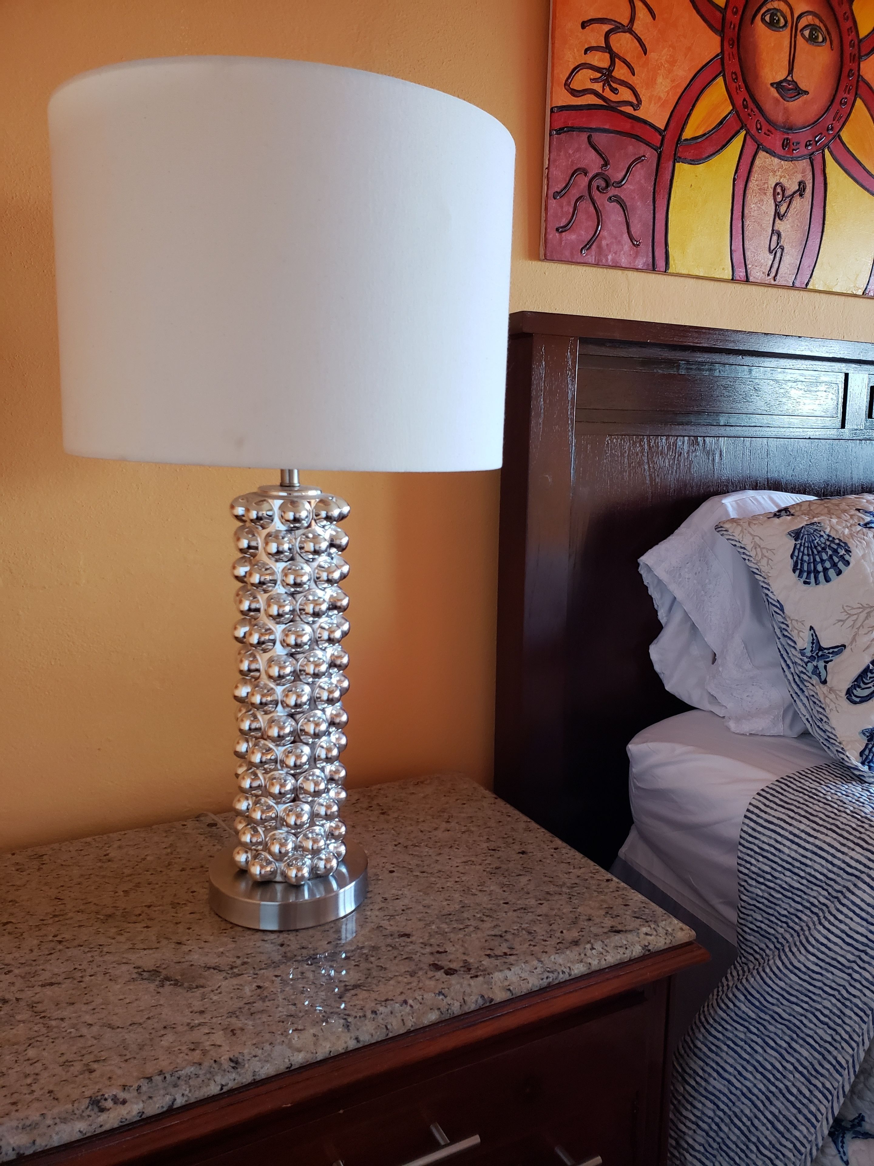 A lamp with a white shade and a metallic base with spherical elements on a granite countertop.
