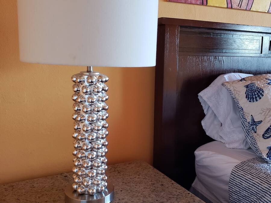 A lamp with a white shade and a metallic base with spherical elements on a granite countertop.