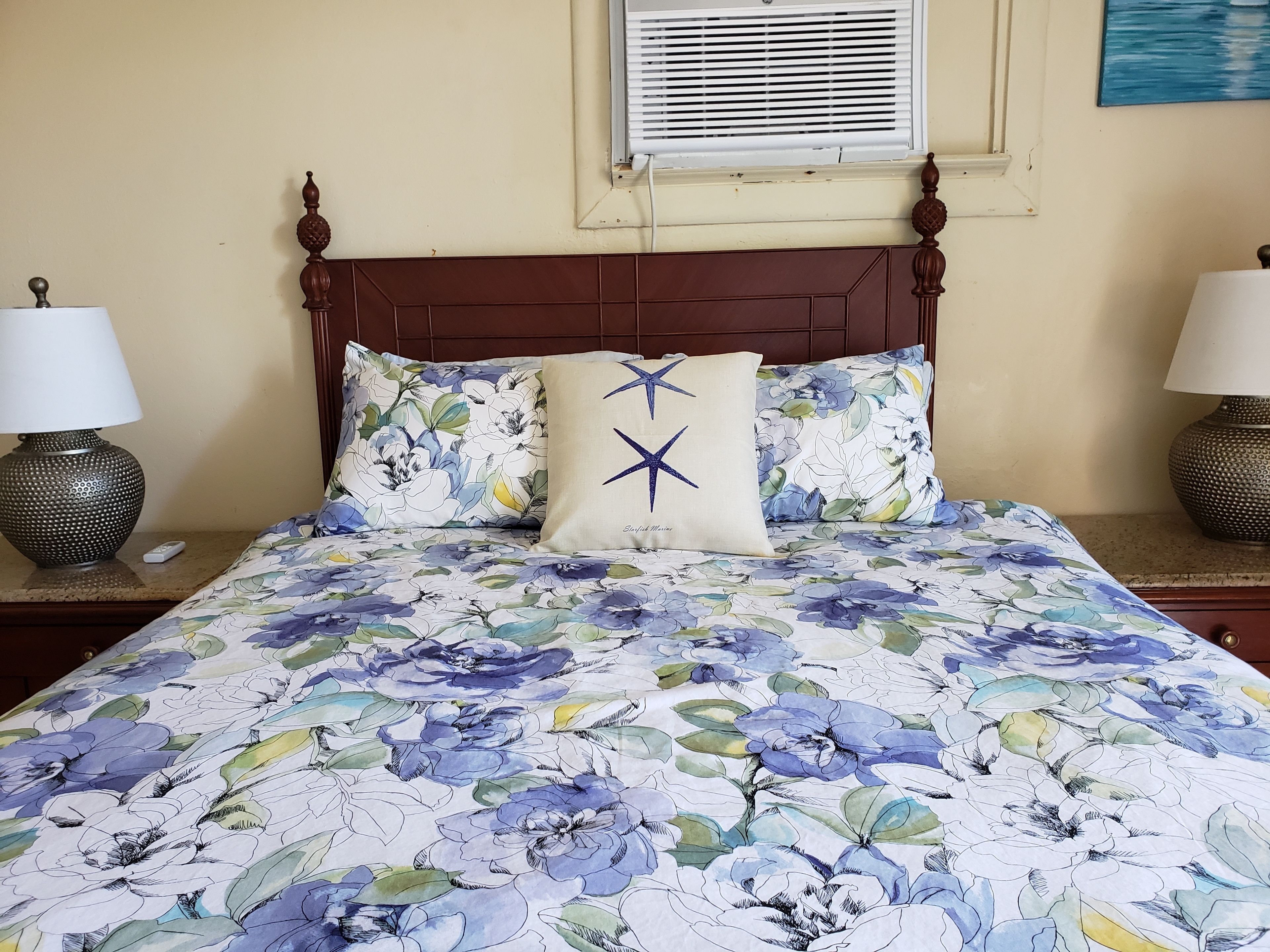 A bed with floral bedding, two bedside lamps, and a window with blinds.