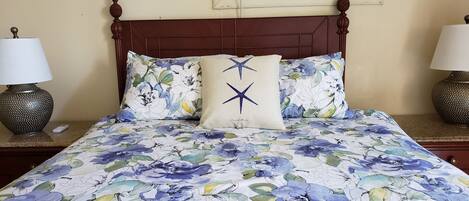 A bed with floral bedding, two bedside lamps, and a window with blinds.