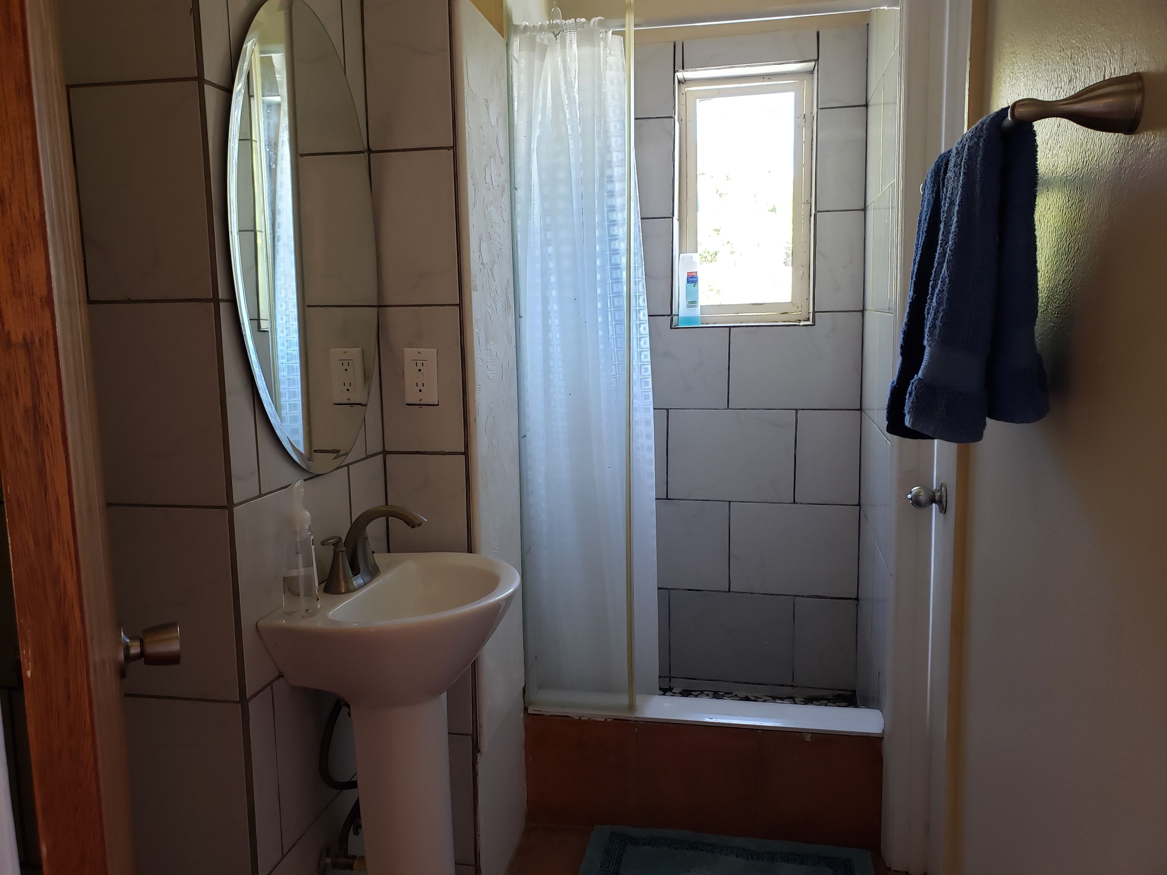 Un baño con lavamanos, espejo, ducha y una toalla colgada en la puerta.