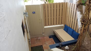 Un petit espace extérieur aménagé avec un banc et une table couverte, une clôture en bois et une porte portant l’inscription « APT. 1 ».