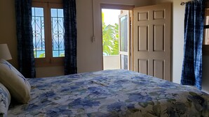 Een slaapkamer met een bed, gordijnen, een raam met uitzicht en een deur naar een buitenruimte.