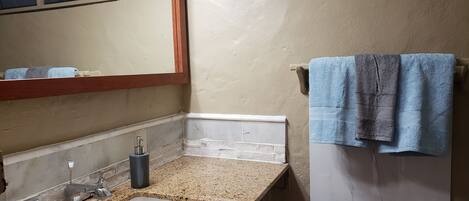 A bathroom with a granite countertop sink, a mirror, and a towel rack with two towels.