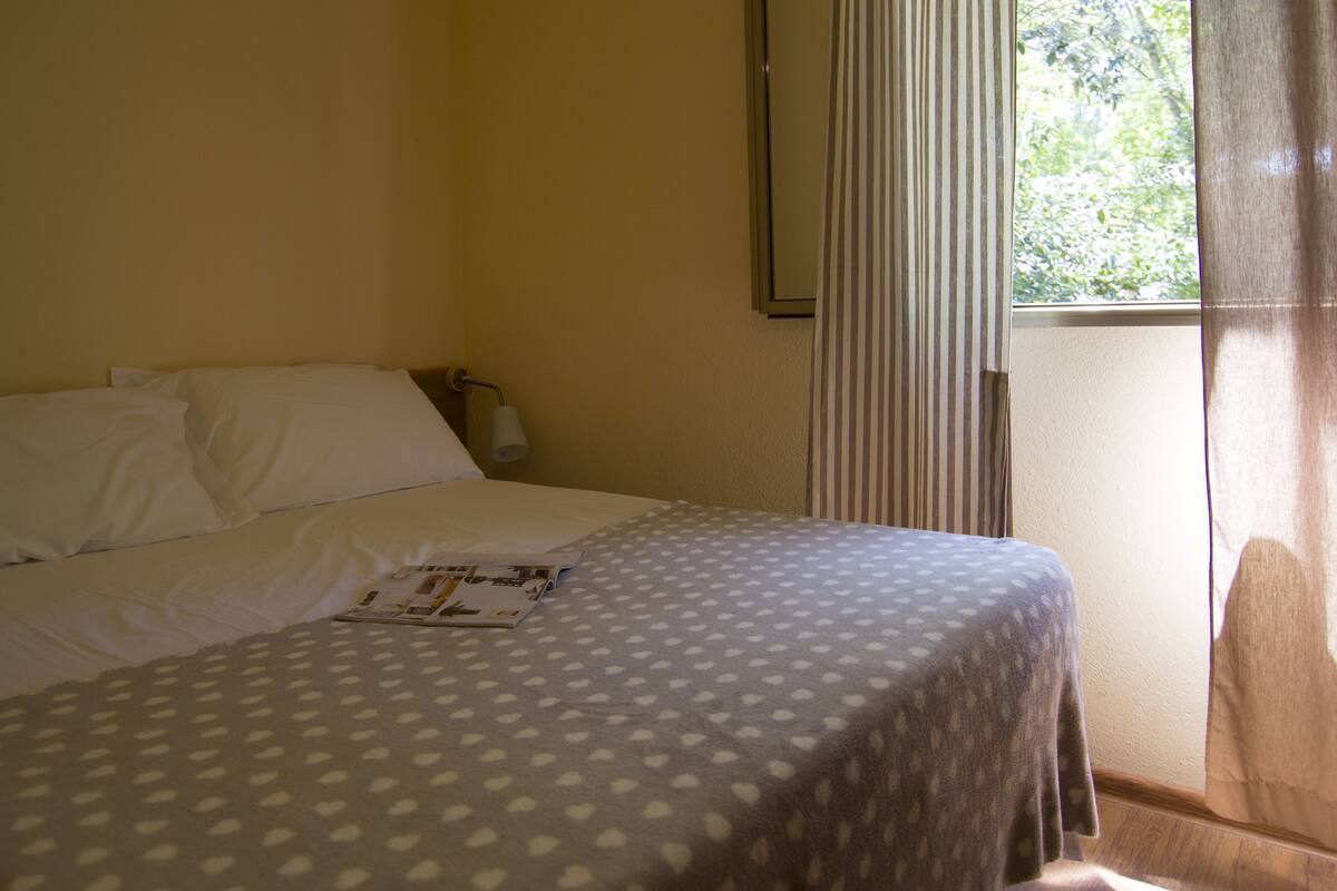 Een hotelkamer met een bed, een raam met gordijnen en een wandlamp.
