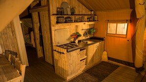 Een landelijke keuken met houten kasten, een gasfornuis en een spoelbak. Er is een raam met gordijnen en een houten plafond.
