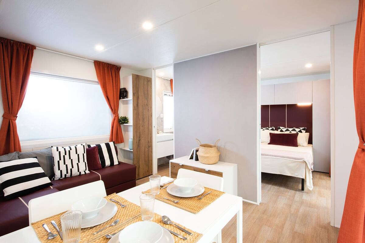 Een moderne, goed verlichte kamer met een eethoek, een bank met gestreepte kussens en een bed met een geometrisch hoofdeinde.