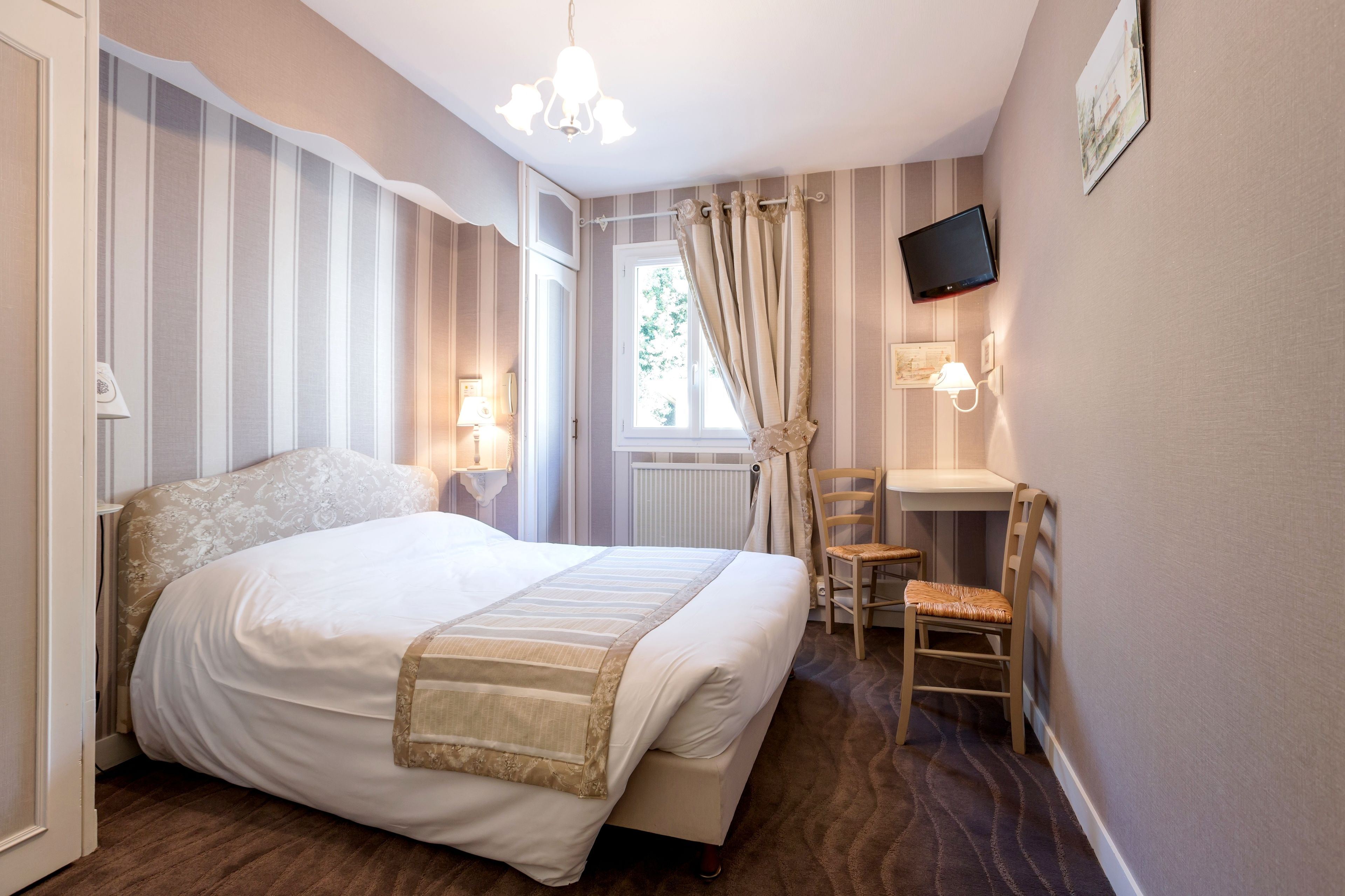A bedroom with a bed, a desk, a chair, a television, and a window with curtains.