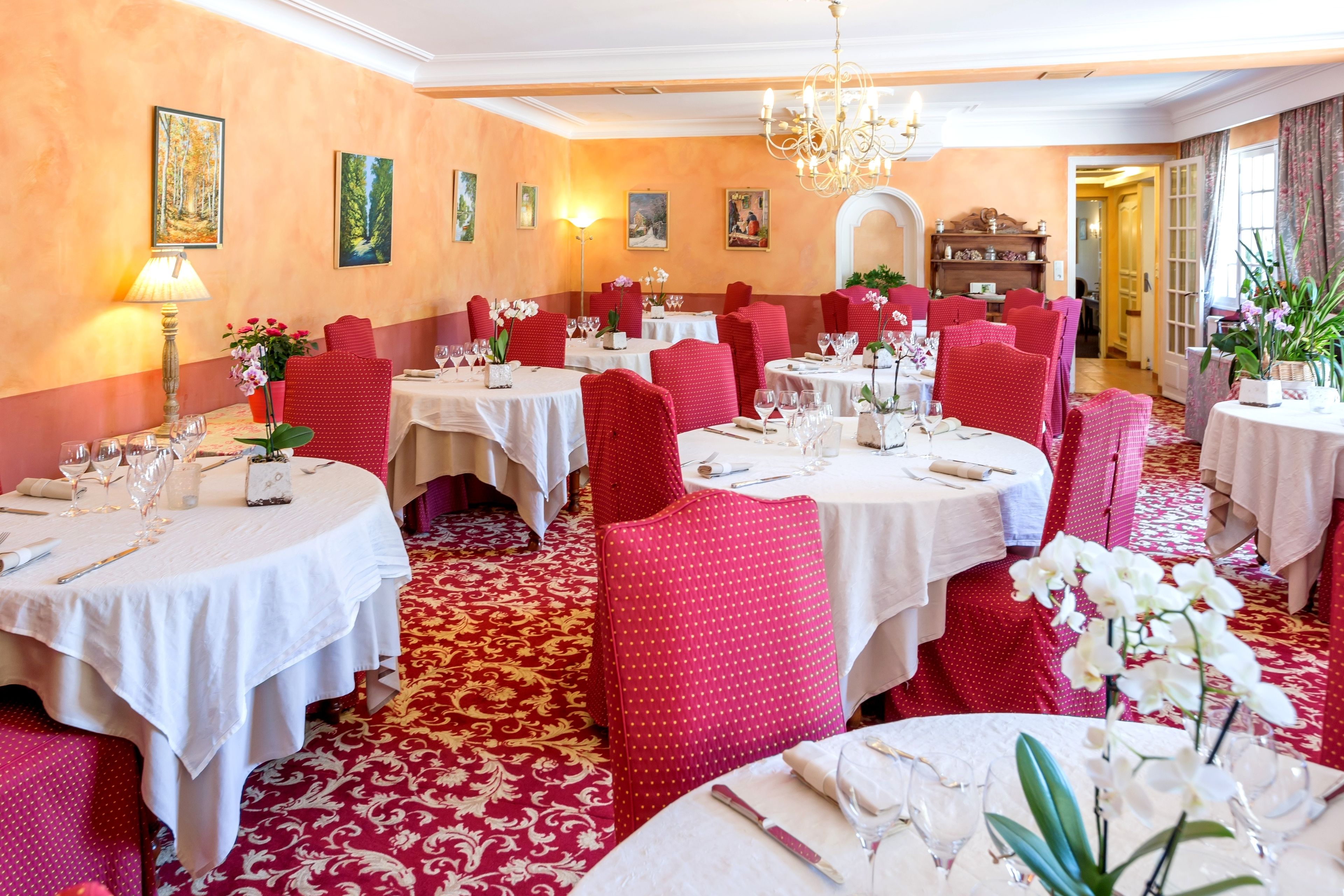 A dining area with round tables, red chairs, and white tablecloths.