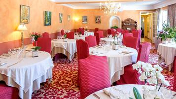A dining area with round tables, red chairs, and white tablecloths.