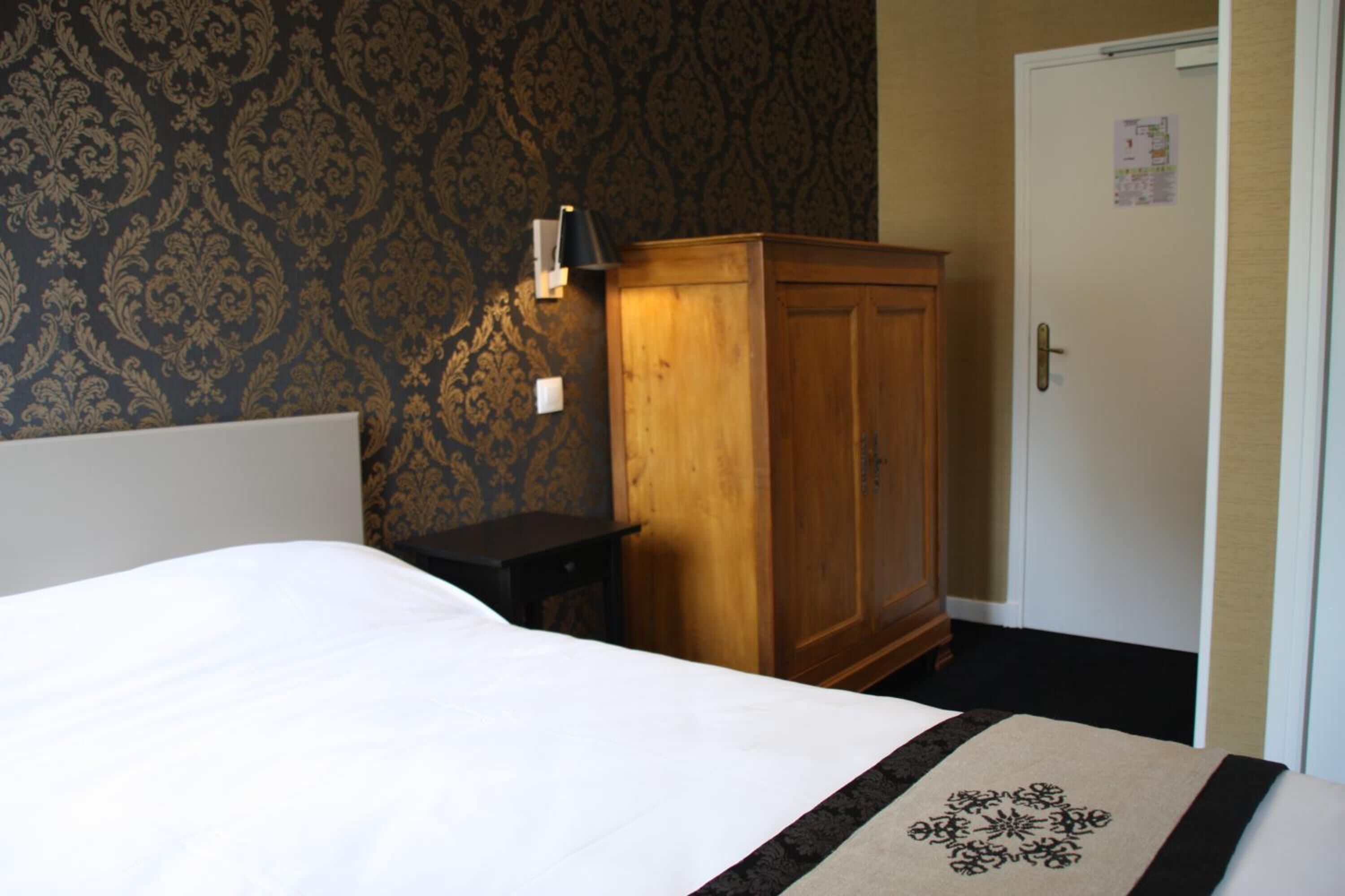 A bedroom with a bed, a wooden wardrobe, a nightstand, and a door with a calendar.