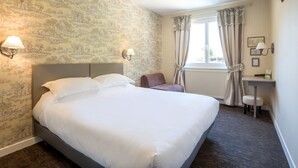 Une chambre d’hôtel avec un grand lit, une chaise, un bureau et une fenêtre avec des rideaux.