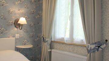 A bedroom with a bed, a nightstand, a wall-mounted lamp, and a window with curtains.