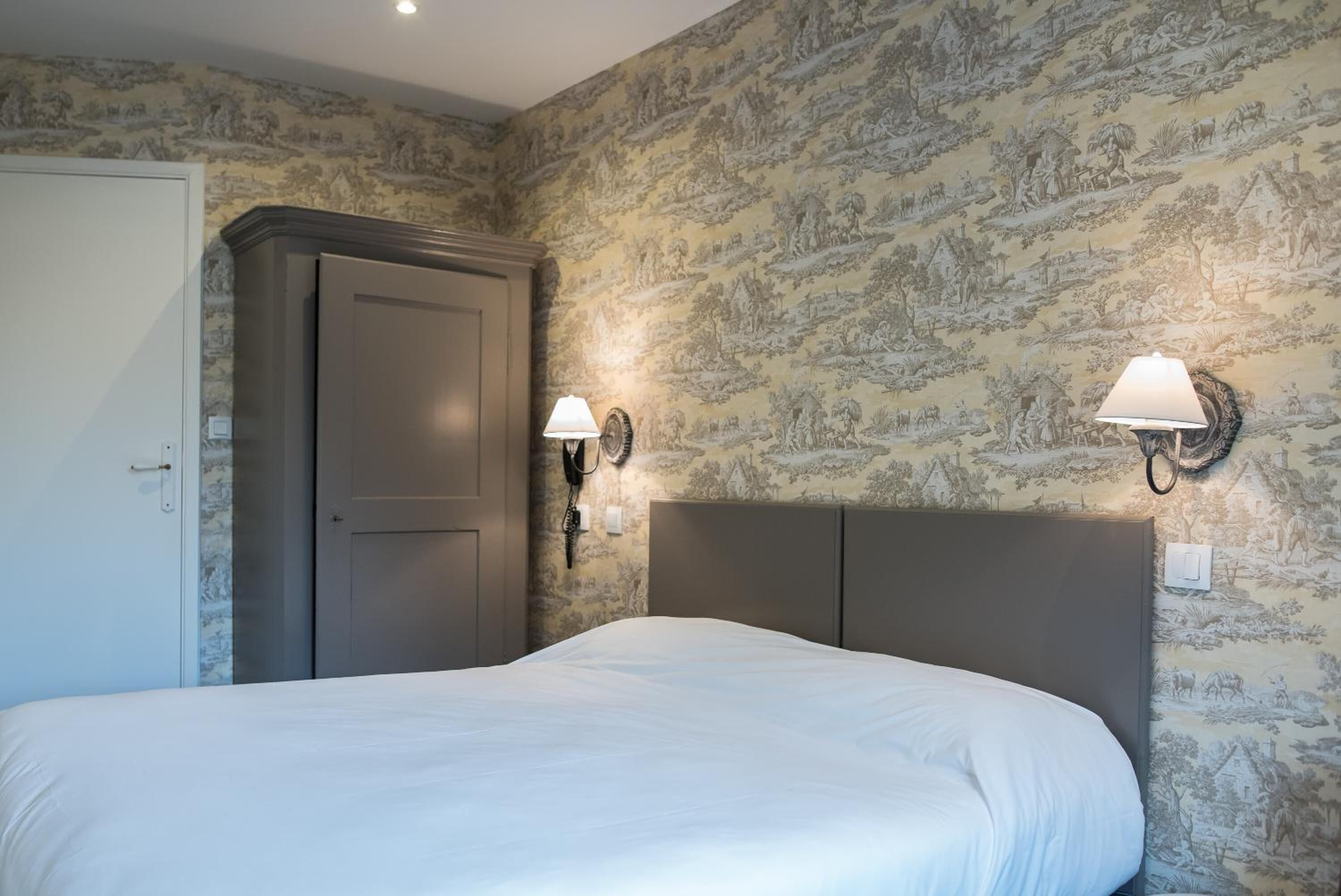 A bedroom with a large bed, a wardrobe, and two wall-mounted lamps.