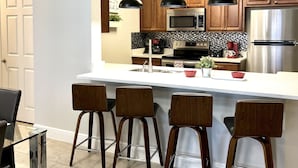 Una cocina moderna con una isla central, taburetes de bar, electrodomésticos de acero inoxidable e iluminación colgante.
