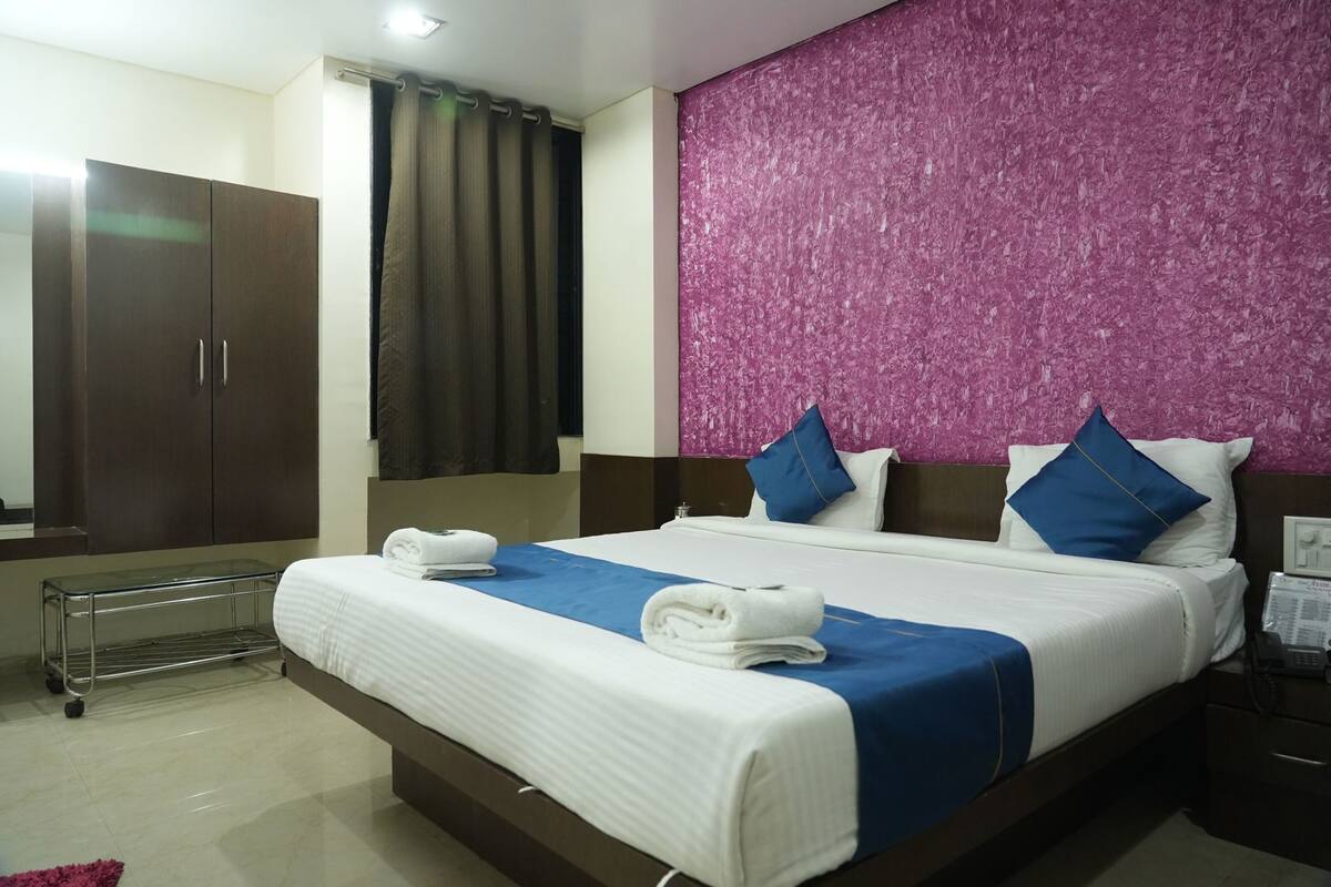 A hotel room with a bed, a wardrobe, a bathroom, and a pink textured wall.