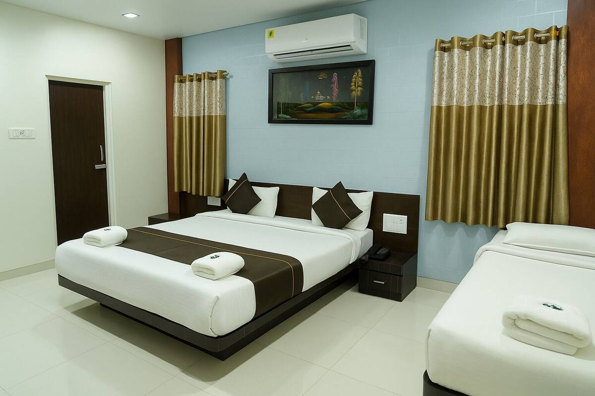 A hotel room with a bed, bedside tables, an air conditioner, a painting, and curtains.