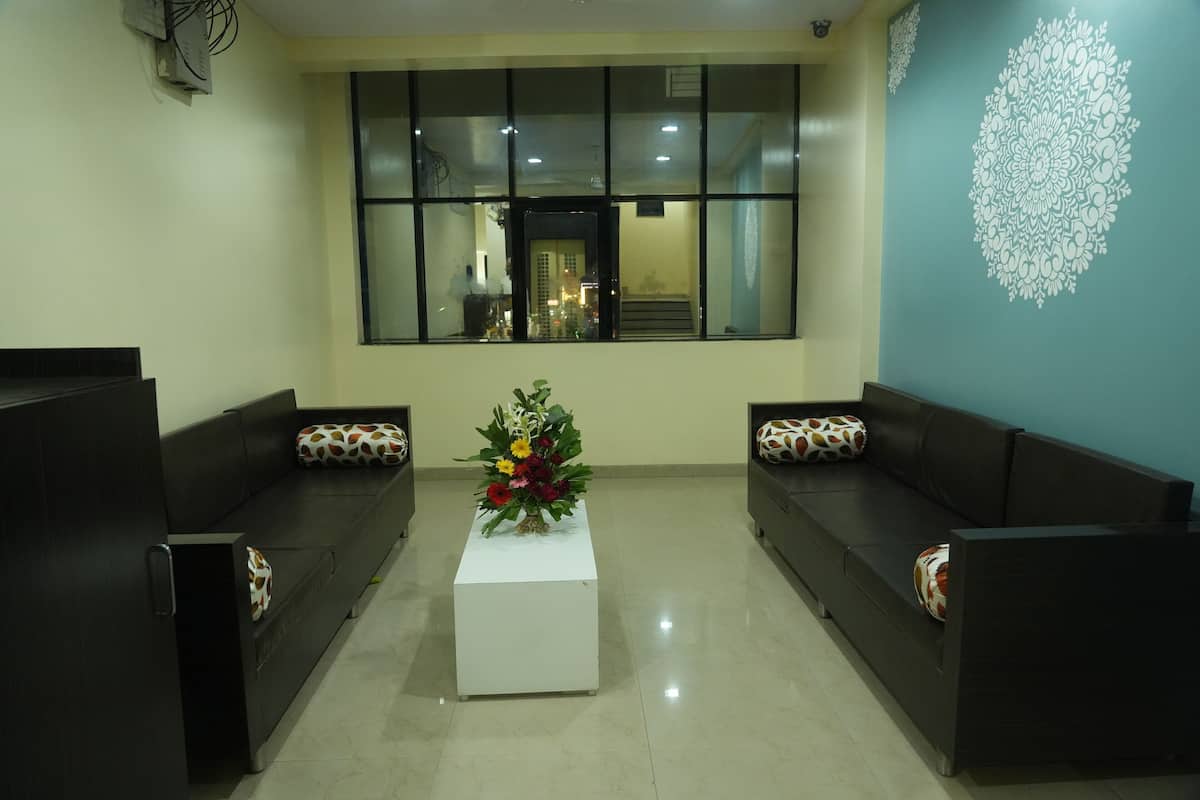 A reception area with a white reception desk, two black sofas with patterned cushions, a floral centerpiece, and a large window with a view of the interior.