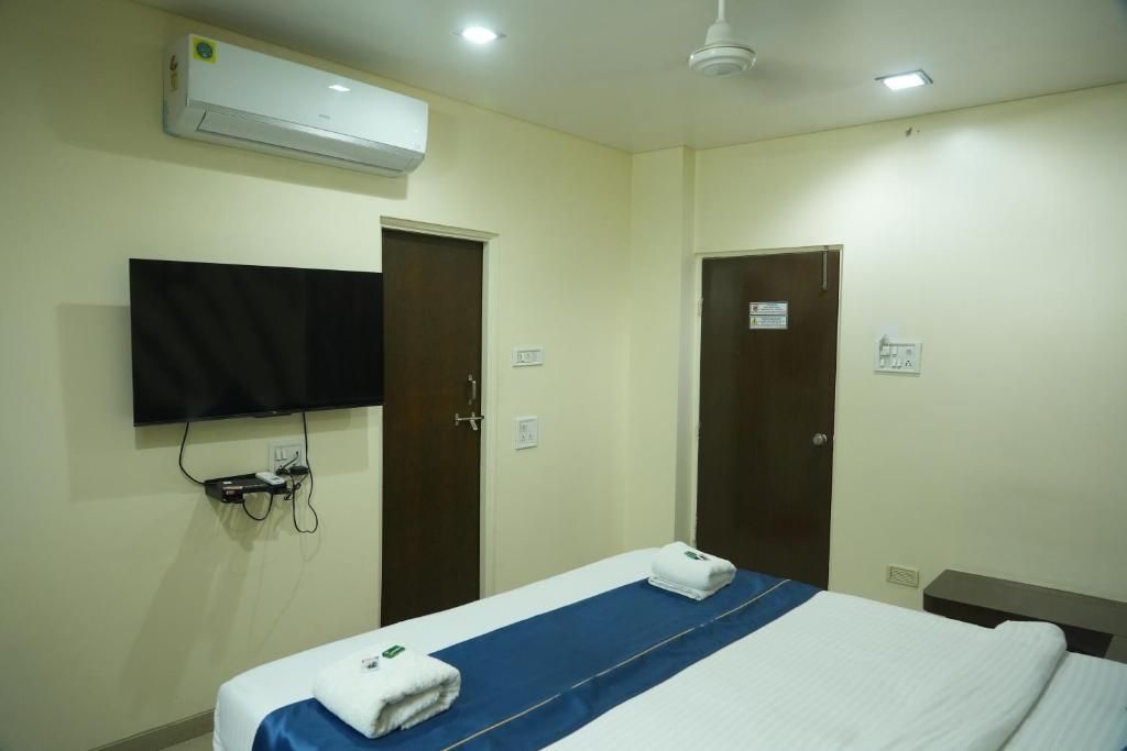 Habitación de hotel con una cama, un televisor de pantalla plana montado en la pared y un equipo de aire acondicionado sobre la cama.
