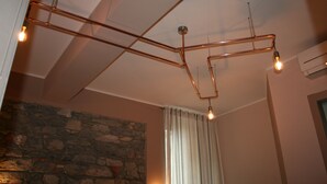 Un soffitto con tubi in rame e lampadine, una parete in pietra e una finestra con tende.
