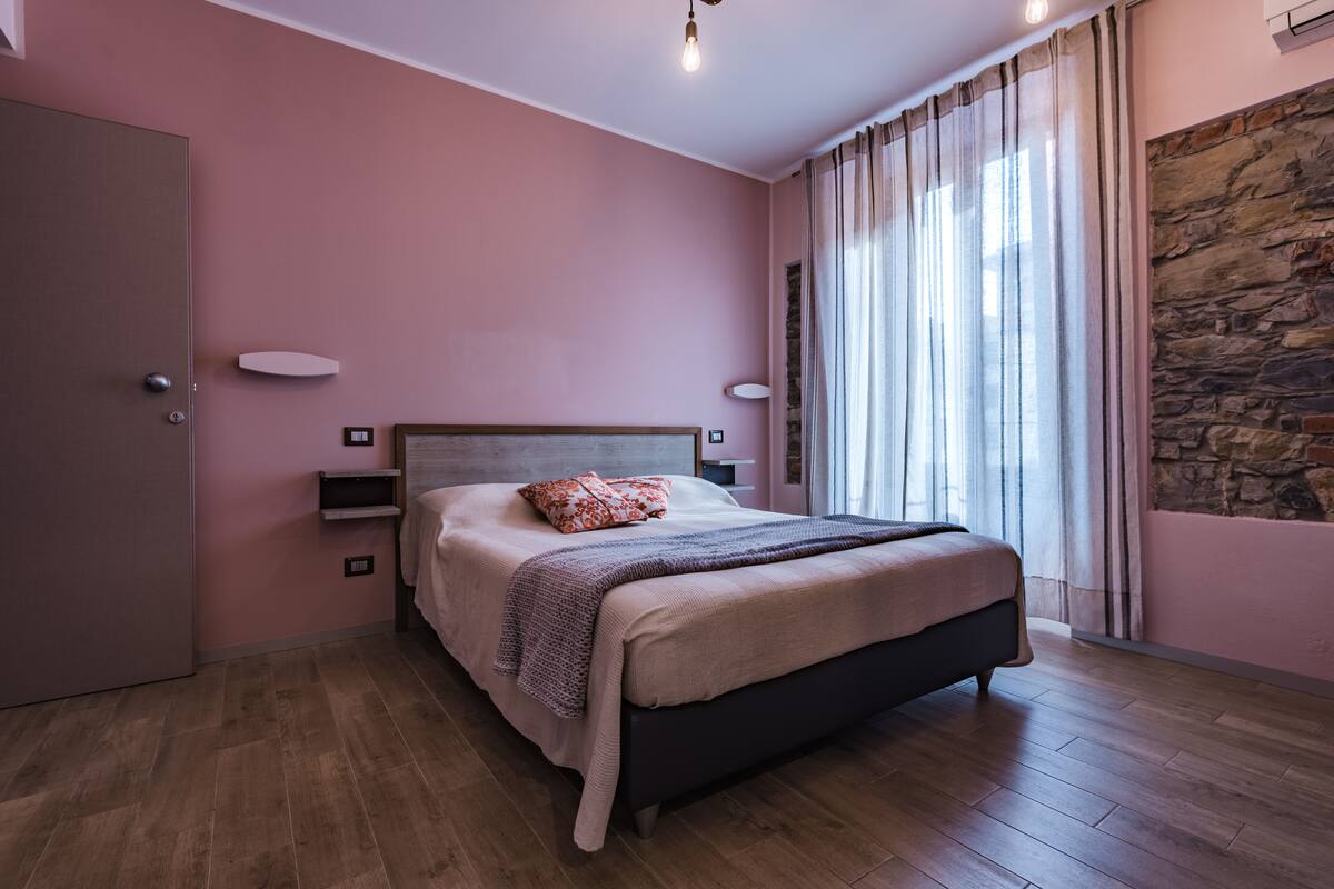 Ein Schlafzimmer mit Bett, Kleiderschrank, Nachttisch, Lampe und einem Fenster mit Vorhängen.
