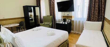 A hotel room with a large bed, a smaller bed, a desk with a chair, a TV, and a mirror.