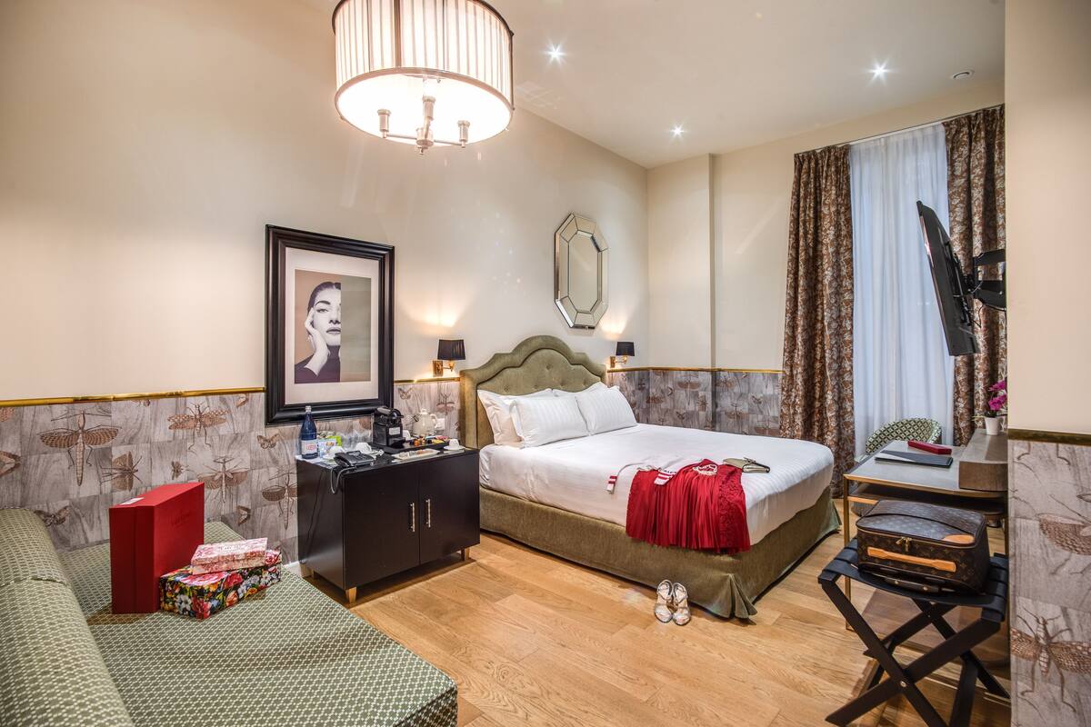 Habitación de hotel con cama, mesita de noche, escritorio, silla y un espejo grande.