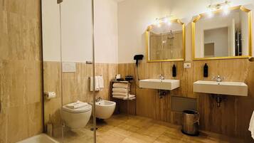 A modern bathroom with a glass-enclosed shower, a bidet, two sinks, and a large mirror with lights.