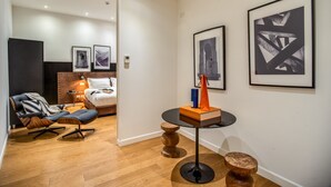 A modern hotel room with a leather chair, a bed, a round table with a book and a bag, and framed artwork on the wall. - The Talent Hotel (Rome)