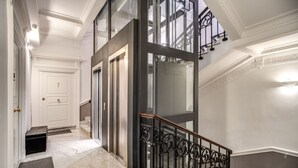 Una gran escalera con escalones de mármol y barandillas negras ornamentales, que conduce a un rellano en el segundo piso con un puerta de vidrio.